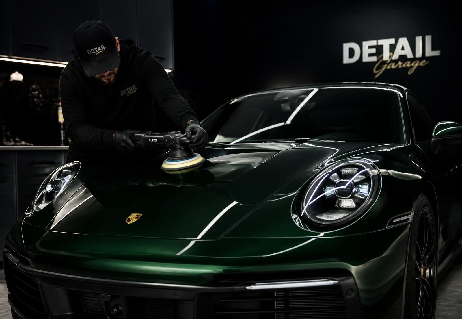 Detailer machine-polishing the hood of a deep green sports car